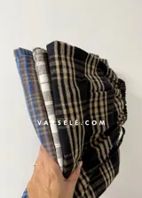 Pantalón tipo palazo de corte amplio y tiro alto, confeccionado en tela con estampado de cuadros escoceses en tonos marrones, blancos y negros. Cuenta con cintura elástica y bolsillos laterales.