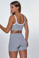 Conjunto deportivo compuesto por un top y un short de tiro alto en color gris. El top presenta breteles blancos, escote redondo y el logo de la marca estampado en el frente. El short cuenta con costuras decorativas blancas que realzan el diseño.