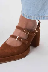 Zapatos de tacón tipo Mary Jane en gamuza color marrón, con doble tira con hebillas metálicas doradas sobre el empeine, punta cuadrada y taco bloque alto.