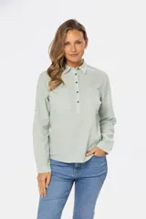 Camisa blanca de manga larga con cuello y tapeta de medio botón. Presenta dos bolsillos frontales con tapa y botones metálicos. Las mangas tienen presillas para sujetar el puño enrollado.