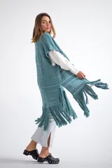 Chaleco largo de tejido de punto color azul verdoso, sin mangas y con flecos en el ruedo. Presenta calados con diseño geométrico.