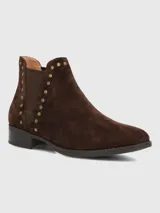 Bota corta tipo chelsea de gamuza color marrón, con detalle de tachas metálicas doradas a lo largo del elástico lateral y tacón bajo cuadrado.