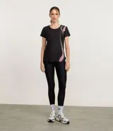 Remera deportiva femenina de manga corta, color negro, confeccionada en microfibra de helanca. Posee escote redondo y estampado localizado en formato de ondas en el lateral delantero en tonos verde, lila y rosado.