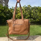 Cartera tipo tote de cuero natural color camel, con textura granulada. Cuenta con doble asa fija para llevar al hombro, correa larga ajustable y removible, cierre superior y bolsillo externo con cierre en la parte trasera.