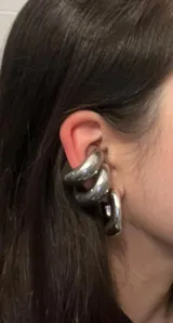 Set de tres piezas de joyería para la oreja, color plateado, con acabado brillante y diseño grueso y orgánico. Incluye un ear cuff que cubre parte de la oreja y dos aros gruesos.