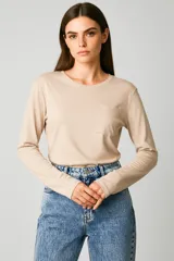 Remera de manga larga color beige claro, corte al cuerpo, con cuello redondo y un bolsillo simple en el pecho.