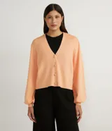 Cárdigan corto color durazno de punto con escote en V, cierre frontal con botones forrados, mangas largas abullonadas y puños acanalados.