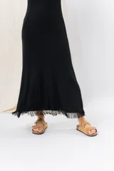 Vestido midi de tejido tipo seda con caída fluida, escote redondo y sin mangas. Presenta un diseño minimalista con detalle de flecos en el ruedo.