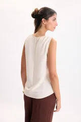 Musculosa con escote en V color crudo, confeccionada en tejido airflow liviano, de corte suelto y sisas amplias.