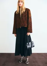 Chaqueta de cuero de potro color marrón con estampado tipo animal print en tonos oscuros, de corte recto y largo recortado. Cuenta con cuello camisero, cierre frontal de cremallera metálica y mangas largas amplias con puños rectos.