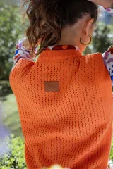 Chaleco tejido de punto calado en color lila, con cuello redondo y hombreras pequeñas. Presenta un diseño sin mangas y textura abierta.