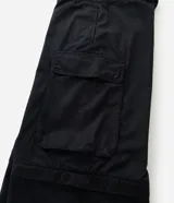 Pantalón cargo de corte mega baggy, color negro, confeccionado en sarga de algodón. Presenta múltiples bolsillos funcionales y un diseño versátil que permite transformar la prenda en bermuda mediante un sistema de ajuste en las piernas.