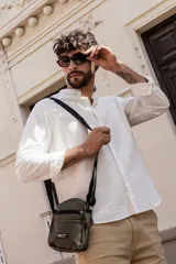 Morral color gris oscuro con correa ajustable negra. Cuenta con un compartimento principal con cierre, un bolsillo frontal con cierre y un bolsillo frontal abierto. Tiene un parche con la inscripción "NOT JUST A BAG. casual and effortless style".