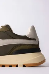 Championes urbanos de diseño técnico, combinando paneles de gamuza y tela en tono verde oliva con detalles en beige y negro. Presentan una suela de plataforma en color crema con base dentada en tono caramelo.
