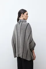 Capa de tejido de punto en color beige y negro con patrón de espiga, cuello alto y cierre de botón. Presenta vivos negros en contraste que delinean el diseño.