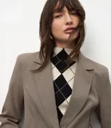 Blazer de sastrería color marrón, con solapas clásicas, cierre frontal de un botón, bolsillos con solapa y mangas largas. Presenta un corte entallado que define la silueta.