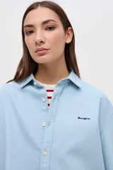 Camisa de algodón en color celeste claro, con cuello solapa, cierre frontal de botones y bordado pequeño en el pecho. Presenta un corte holgado y mangas largas.