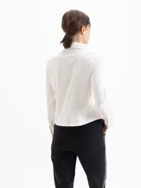 Camisa de jacquard con diseño de flores sutiles, color blanco, con cuello amplio de puntas marcadas, mangas largas con puños y cierre frontal con botones.