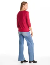 Buzo de tejido fino en color blanco, con cuello redondo y mangas tres cuartos tipo raglán. Presenta un detalle decorativo de tachas metálicas a lo largo de las mangas.