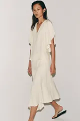 Falda midi de tiro medio, color blanco off-white, confeccionada en hilatura de viscosa. Presenta un diseño fluido, con bajo asimétrico y detalle de caída drapeada en el lateral. Cierre con cremallera oculta en costura.