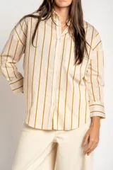Camisa de corte oversize con estampado de rayas verticales en tonos verde, blanco y ocre. Presenta cuello clásico, cierre frontal con botones, bolsillo en el pecho y mangas largas con puños abotonados.