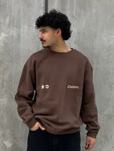 Buzo marrón con logo "Osten" y diseño gráfico de sol en color beige. Corte oversize, cuello redondo y mangas largas.