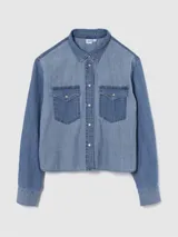Camisa de jean de corte corto con diseño de paneles en dos tonos de azul. Presenta cuello clásico, cierre frontal con botones metálicos y dos bolsillos delanteros con solapa.