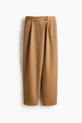 Pantalón sastrero de corte holgado en color tostado, con diseño asimétrico cruzado en la cintura, botón frontal y pliegues en las piernas.