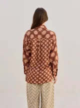 Camisa de algodón con estampado geométrico de ondas en tonos marrón y negro, corte holgado, mangas largas y cuello clásico.