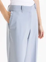 Pantalón de vestir tiro alto color celeste, de corte wide leg y largo hasta el suelo, con bolsillos delanteros decorados con volados tableados y bolsillos ojal en la espalda.