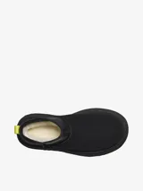 Bota corta tipo botineta de la marca UGG, color negro, con diseño de caña baja y plataforma elevada. Presenta una tira de agarre en color amarillo neón en la parte posterior y una suela de goma gruesa con textura acanalada.