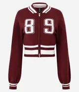 Cardigan de punto estilo college color bordó, con cierre frontal de doble cremallera, mangas largas y detalles de rayas blancas en cuello, puños y ruedo. Presenta una estampa numérica blanca en el frente.