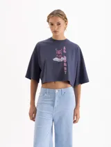 Remera blanca de corte cropped y manga corta, confeccionada en algodón. Presenta una estampa frontal con un conejo con estampado animal print sobre una nube y el texto 'IL BUNNY' en color amarillo.