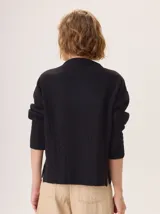 Buzo de lana color beige con cuello chimenea, mangas largas y diseño de tejido trenzado en la parte inferior y puños.