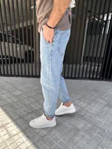 Pantalón jeans slouchy de hombre, en tono azul claro, con diseño de corte holgado en las piernas y botamangas ligeramente ajustadas o dobladas.