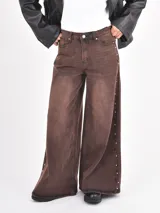 Jean de corte wide leg en color óxido con efecto lavado. Presenta una abertura lateral decorada con pequeñas tachas metálicas a lo largo de toda la pierna.