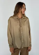 Camisa color marrón claro de corte holgado, con cuello clásico, cierre frontal con botones y mangas largas.