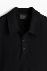 Remera polo negra de manga corta con cuello clásico, tapeta de botones y corte ajustado.