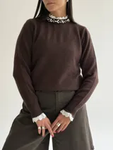 Sweater de punto color beige, con cuello redondo adornado con apliques de pedrería y detalle de puntilla blanca en el cuello y los puños.