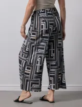 Pantalón ancho estilo palazzo, de seda fría plisada con estampado geométrico en negro, blanco y beige. Tiene pretina ancha elastizada y largo crop.