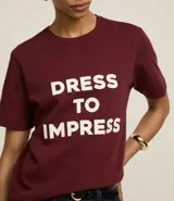 Remera color borgoña de algodón, con cuello redondo y mangas cortas. Estampa frontal con la frase "Dress to Impress" en letras mayúsculas blancas.