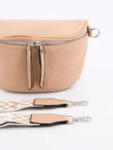 Riñonera negra de cuero con forma curva y cierre superior de cremallera metálica plateada. Presenta tiradores de cuero colgantes en los cursores y anillas metálicas a los lados para sujetar la correa.