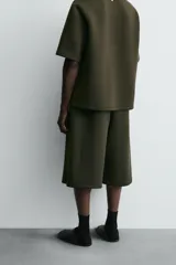 Bermuda de corte oversize confeccionada en tejido técnico compacto con elasticidad. Presenta cintura elástica ajustable con cordón, pinzas en el delantero y la espalda, y bolsillos laterales.