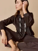 Campera de corte holgado con textura aterciopelada y estampado de cuadros sutil. Presenta cuello con cordones ajustables, cierre frontal con botones y mangas largas con puños elásticos.