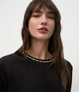 Remera de corte regular confeccionada en gamuza sintética color negro, con mangas cortas y cuello redondo decorado con una aplicación de pedrería brillante.