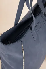 Bolso tipo tote color marrón con tachas plateadas en los bordes y monedero colgante con cierre.