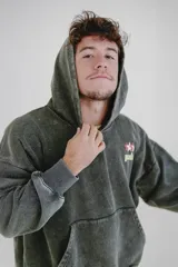 Canguro gris oscuro con efecto lavado (acid wash) y capucha. Presenta un pequeño estampado frontal con estrellas y la palabra "pulau" en tonos rosado y amarillo. Tiene bolsillo canguro y puños acanalados.