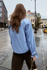 Camisa corta de manga larga, color celeste con finas rayas blancas verticales. Posee cuello solapa y puños anchos ajustados con lazos del mismo tejido.