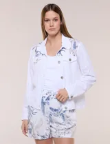 Campera liviana de lino color blanco, con estilo denim y silueta semi entallada. Presenta un canesú superior estampado con motivos florales en tonos azules y tostados, cuello camisero, abotonadura frontal con botones rústicos y bolsillos con solapa en el pecho.