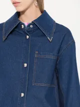 Camisa de denim azul con costadillos y bajo mangas en denim azul marino, punteras metálicas níquel en puntas de cuello, broches semi esfera níquel en centro delantero y puños, bordado JCH de hilo a contra tono en ruedo del lado derecho.